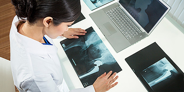 Female Woman Hospital Doctor Looking at X-Rays & Laptop